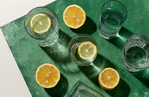 drink, detox and diet concept - glasses with water and lemons on emerald green background
