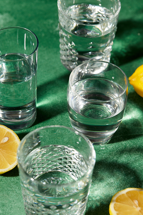 drink, detox and diet concept - close up of glasses with water and lemons on emerald green background