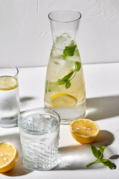 drink, detox and diet concept - glasses with fruit water or lemonade, lemons and peppermint on white table