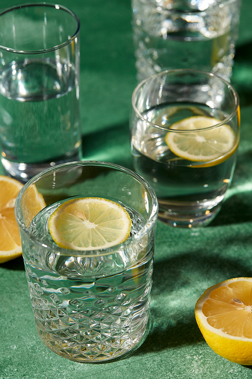 drink, detox and diet concept - close up of glasses with water and lemons on emerald green background