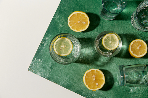 drink, detox and diet concept - glasses with water and lemons on emerald green background