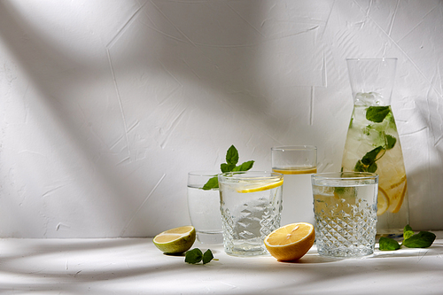 drink, detox and diet concept - glasses with fruit water or lemonade, lemons, limes and peppermint on white table