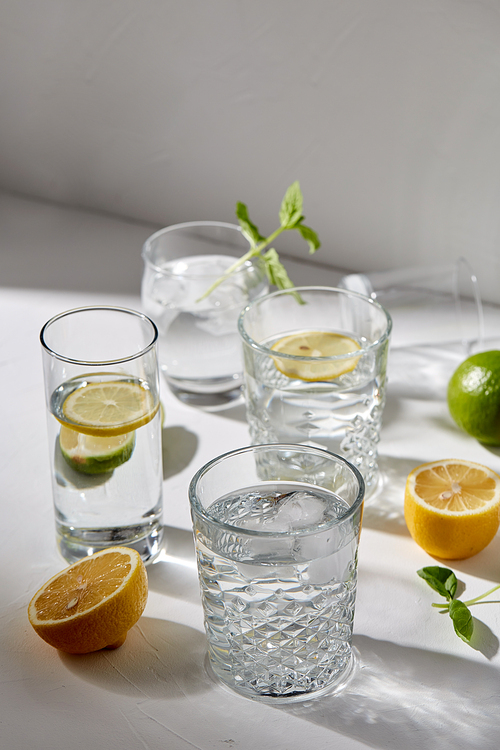 drink, detox and diet concept - glasses with fruit water or lemonade, lemons, limes and peppermint on white table