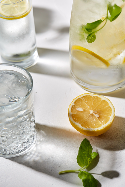 drink, detox and diet concept - glasses with fruit water or lemonade, lemon and peppermint on white table