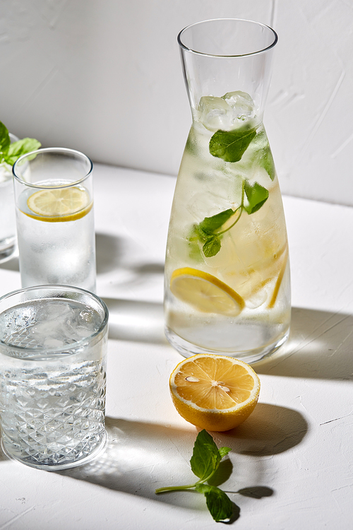drink, detox and diet concept - glasses with fruit water or lemonade, lemons and peppermint on white table