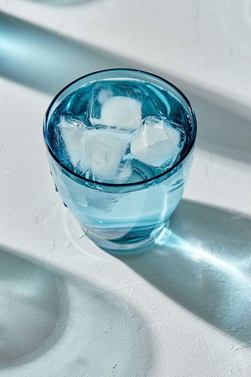 drink, detox and diet concept - blue glass of cold water with ice cubes on white background