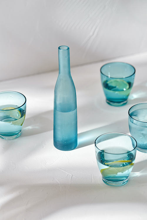 drink, detox and diet concept - blue glasses with water, lemons and ice on white background