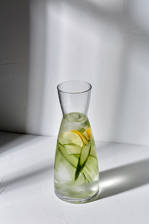 drink, detox and diet concept - glass bottle of fruit water or lemonade with lemon and cucumber dropping shadows on white surface