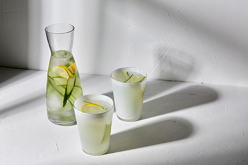 drink, detox and diet concept - glasses with fruit water or lemonade with lemon and cucumber dropping shadows on white surface