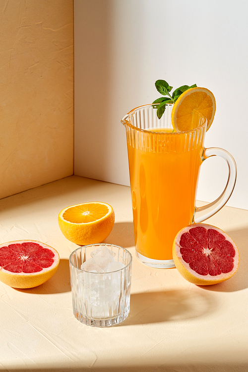 drink, detox and diet concept - jug with orange juice, cut grapefruit and ice cubes in glass on table