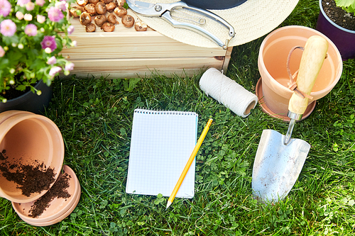 gardening and people concept - notebook with pencil, garden tools, wooden box and flowers in pots at summer