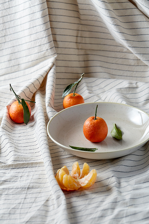 food, healthy eating and fruits concept - close up of mandarins on plate over drapery