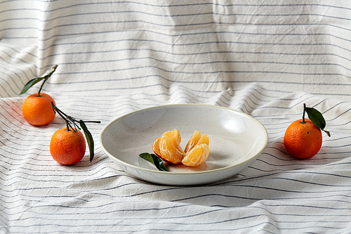 food, healthy eating and fruits concept - close up of mandarins on plate over drapery