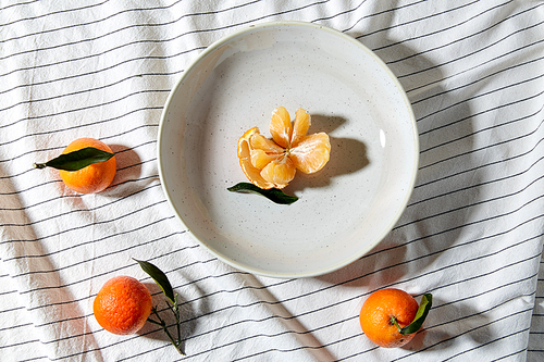 food, healthy eating and fruits concept - close up of mandarins on plate over drapery