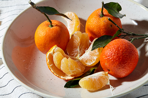 food, healthy eating and fruits concept - close up of mandarins on plate over drapery