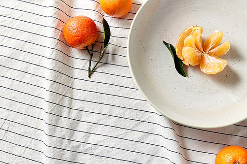 food, healthy eating and fruits concept - close up of mandarins on plate over drapery