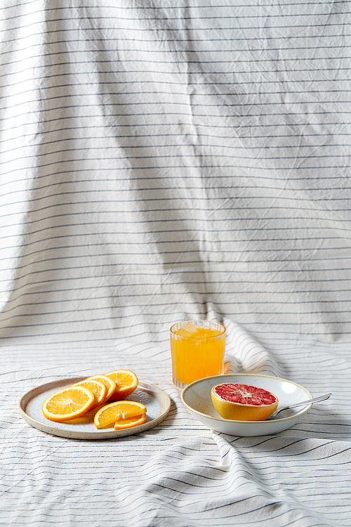 food, healthy eating and fruits concept - still life of grapefruit, sliced orange and glass of juice over drapery