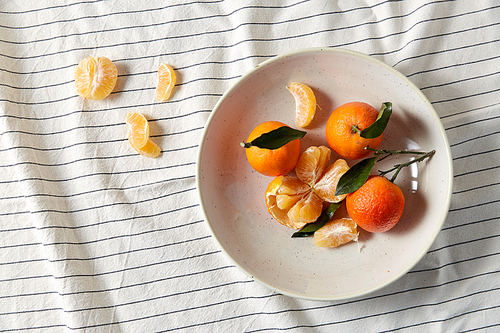 food, healthy eating and fruits concept - close up of mandarins on plate over drapery
