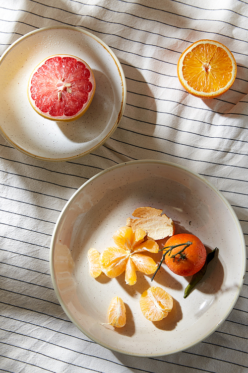 food, healthy eating and fruits concept - close up of mandarin, grapefruit and orange on plates over drapery