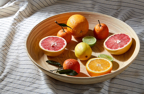 food, healthy eating and vegetarian concept - close up of citrus fruits on wooden plate