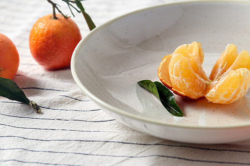 food, healthy eating and fruits concept - close up of mandarins on plate over drapery
