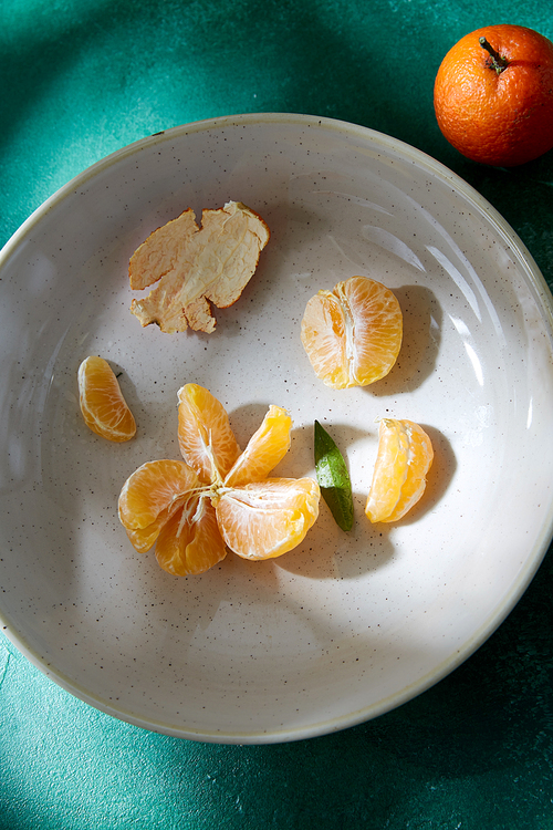 food, healthy eating and fruits concept - still life with peeled mandarins on plate on green background