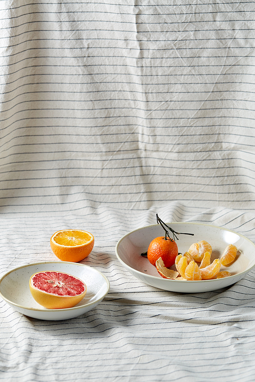 food, healthy eating and fruits concept - close up of mandarin, grapefruit and orange on plates over drapery