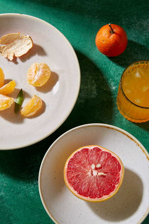 food, healthy eating and fruits concept - still life with mandarins, grapefruit and glass of juice on green background