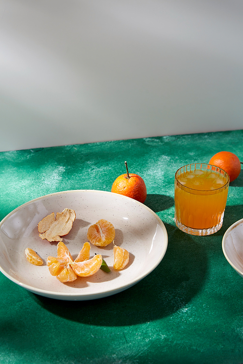 food, healthy eating and fruits concept - still life with peeled mandarins on plate and glass of juice on green background