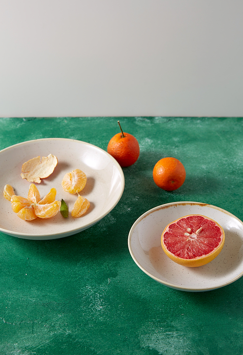 food, healthy eating and fruits concept - still life with peeled mandarins and grapefruit on plates on green background