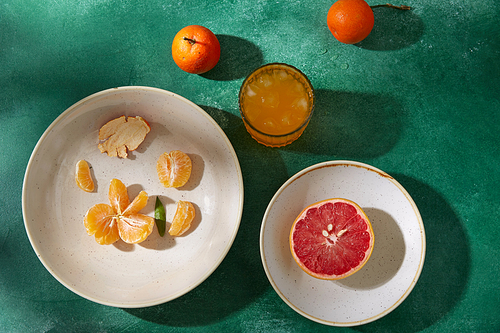 food, healthy eating and fruits concept - still life with mandarins, grapefruit and glass of juice on green background