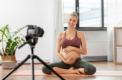 sport and people concept - happy pregnant woman or Vlog with camera on tripod recording online yoga class at home