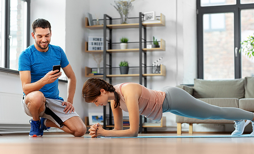 fitness, sport, training and lifestyle concept - happy smiling personal trainer with smartphone and woman doing plank at home