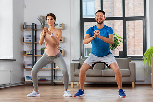 sport, fitness, lifestyle and people concept - smiling man and woman exercising and doing squats at home