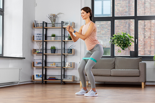 sport, fitness, lifestyle and people concept - happy woman exercising with resistance band at home