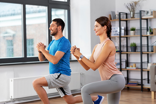 sport, fitness, lifestyle and people concept - smiling man and woman exercising and doing squats in low lunge at home