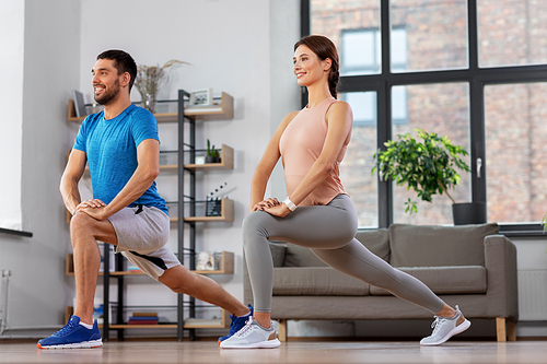 sport, fitness, lifestyle and people concept - smiling man and woman exercising and doing lunge at home