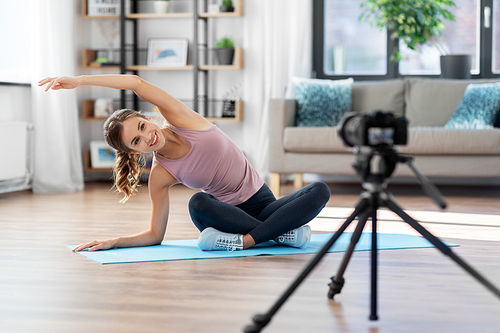 fitness, sport and video blogging concept - woman or Vlog with camera streaming online yoga class at home
