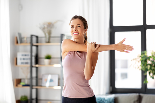 sport, fitness and healthy lifestyle concept - smiling young woman stretching arm at home