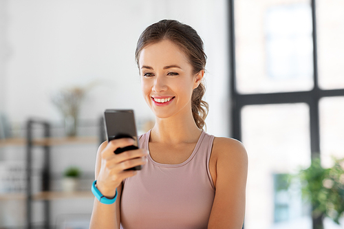 sport, fitness and technology concept - happy smiling young woman with smatphone exercising at home