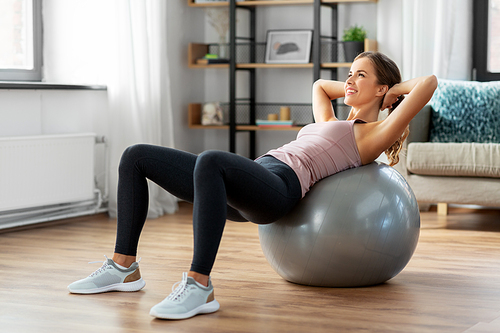 sport and healthy lifestyle concept - happy woman exercising on fitness ball at home