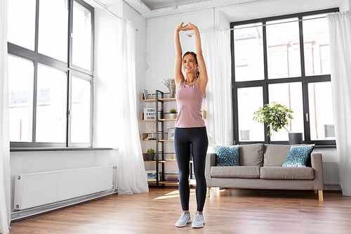 sport, fitness and healthy lifestyle concept - smiling young woman stretching arms at home