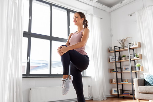 sport, fitness and healthy lifestyle concept - smiling young woman stretching leg at home