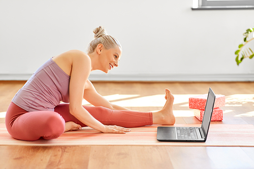 fitness, technology and healthy lifestyle concept - woman with laptop computer exercising at yoga studio