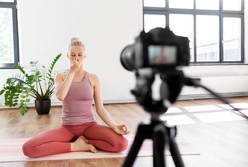 fitness, sport and video blogging concept - woman or Vlog with camera on tripod recording online yoga class in gym or studio