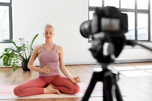 fitness, sport and video blogging concept - woman or Vlog with camera on tripod recording online yoga class in gym or studio