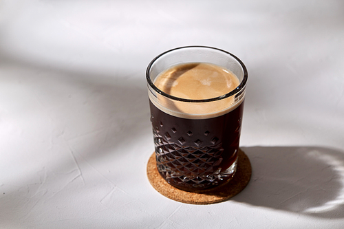 caffeine, objects and drinks concept - glass of coffee on cork drink coaster