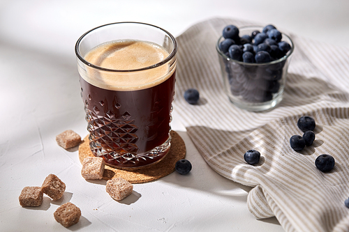 caffeine, objects and drinks concept - glass of coffee on cork drink coaster, brown sugar and blueberries