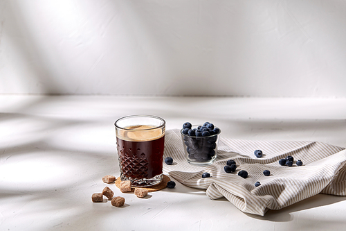 caffeine, objects and drinks concept - glass of coffee on cork drink coaster, brown sugar and blueberries