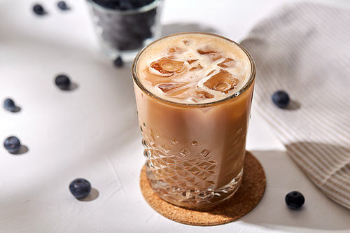 caffeine, objects and drinks concept - glass of ice coffee on cork drink coaster and blueberries